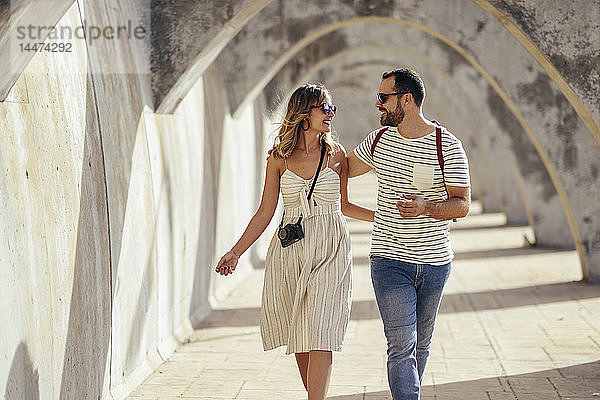 Spanien  Andalusien  Malaga  glückliches Touristenpaar beim Spaziergang unter einem Torbogen in der Stadt