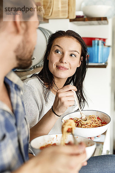 Glückliches Paar sitzt in der Küche und isst Spaghetti
