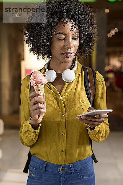 Porträt einer Frau mit Eistüte  die auf ihr Handy schaut