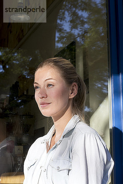 Porträt einer lächelnden Frau vor dem Fenster  die in die Ferne schaut