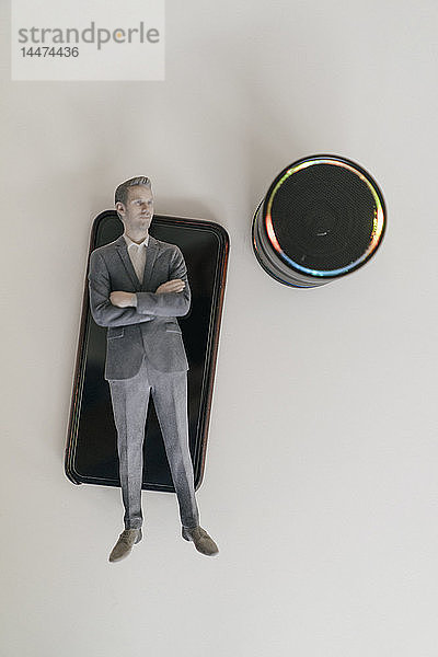 Miniatur-Geschäftsmann-Figur auf dem Smartphone liegend neben dem Lautsprecher des Smart Home