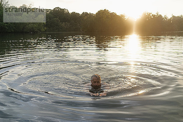 Älterer Mann schwimmt bei Sonnenuntergang in einem See