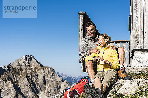 Wanderndes Ehepaar sitzt vor der Berghütte und macht eine Pause