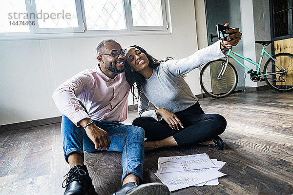 Lächelnder Geschäftsmann und Geschäftsfrau  die auf dem Boden sitzen und sich ein Selfie nehmen