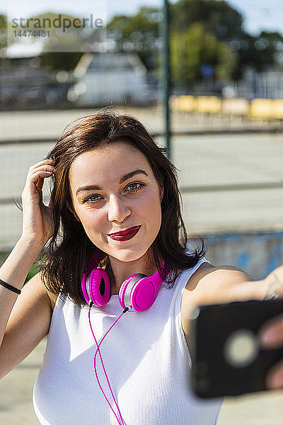Porträt einer lächelnden jungen Frau mit Kopfhörer und Handy in der Stadt