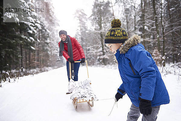 Kleiner Junge und sein Vater mit Schlitten im Winterwald