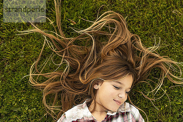 Lächelndes Mädchen mit langen Haaren auf einer Wiese liegend