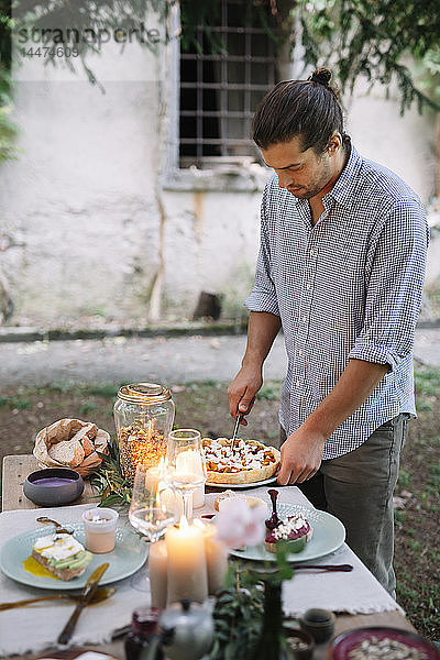 Mann arrangiert ein romantisches Essen bei Kerzenlicht im Freien