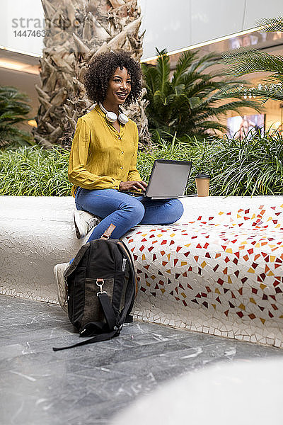 Porträt einer lächelnden Frau  die mit einem Laptop auf einer Bank sitzt