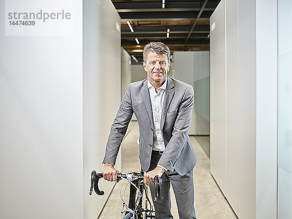 Porträt eines lächelnden Geschäftsmannes mit Fahrrad auf der Büroetage