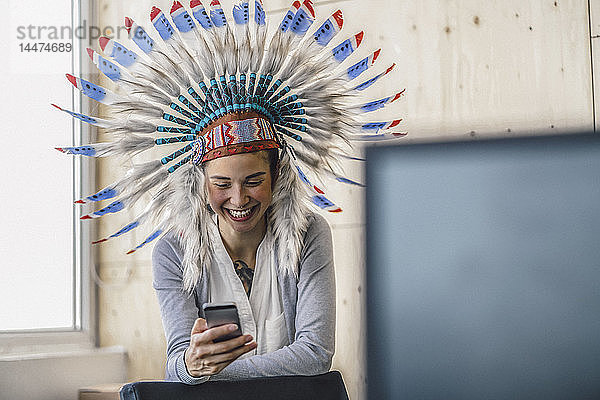 Junge Frau mit indischem Kopfschmuck  steht im Büro und benutzt ein Smartphone