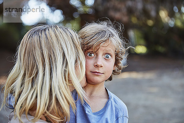 Porträt eines Jungen mit großen Augen  der von seiner Mutter geküsst wird