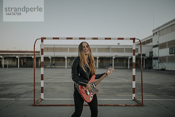 Porträt einer glücklichen jungen Frau  die auf dem Sportplatz Gitarre spielt