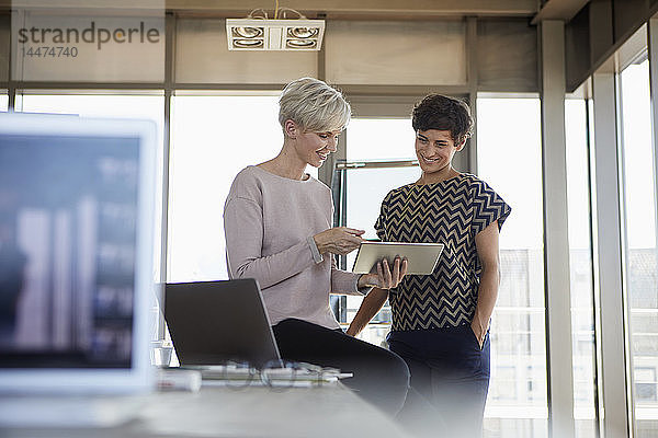 Zwei lächelnde Geschäftsfrauen teilen sich im Büro ein Tablett