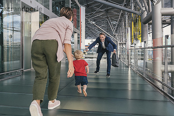 Glückliches Kind rennt auf dem Flughafen in die Arme eines reisenden Geschäftsmannes