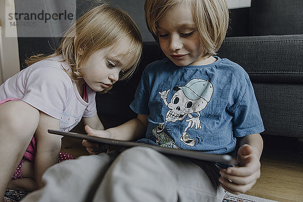 Bruder und kleine Schwester sitzen zu Hause auf dem Boden und benutzen ein digitales Tablett