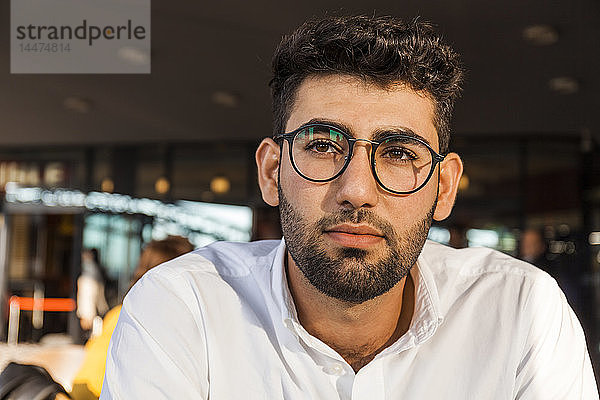 Porträt eines nachdenklichen jungen Geschäftsmannes mit Bart und Brille im Straßencafé