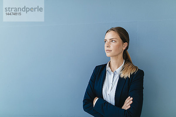 Porträt einer jungen Geschäftsfrau vor blauem Hintergrund  die skeptisch schaut