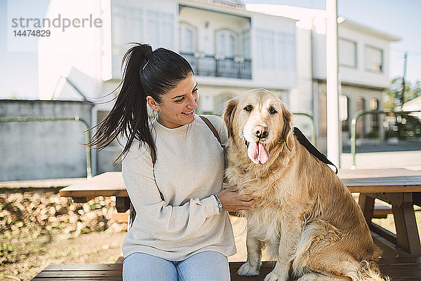 Lächelnde junge Frau mit ihrem im Freien ruhenden Golden-Retriever-Hund