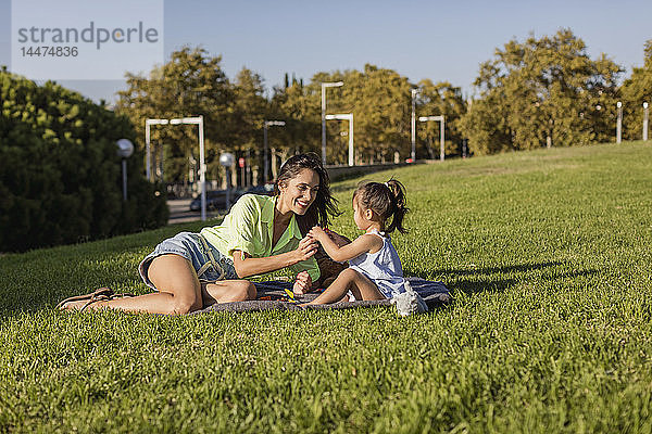 Glückliche Mutter spielt mit Tochter auf einer Decke im Park