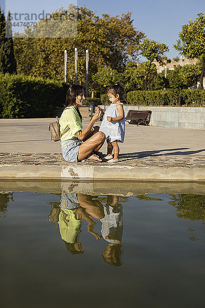 Glückliche Mutter mit Tochter an einem Pool in einem Park