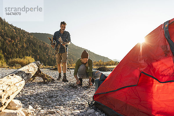 Ein erwachsenes Paar zeltet am Flussufer und sammelt Holz für ein Lagerfeuer