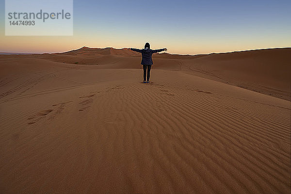 Marokko  Rückenansicht einer Frau  die in der Dämmerung auf einer Wüstendüne sitzt