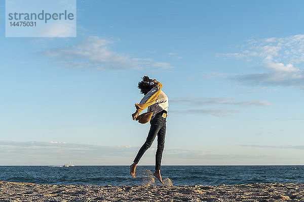 Frau springt am Strand  trägt Kopfhörer  hört Musik