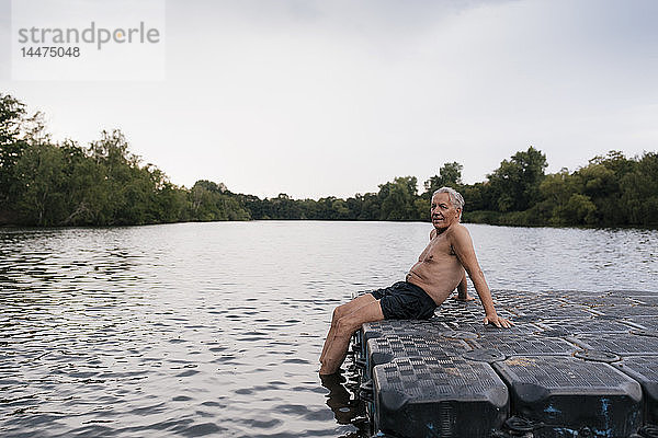 Älterer Mann sitzt auf einem Floß in einem See
