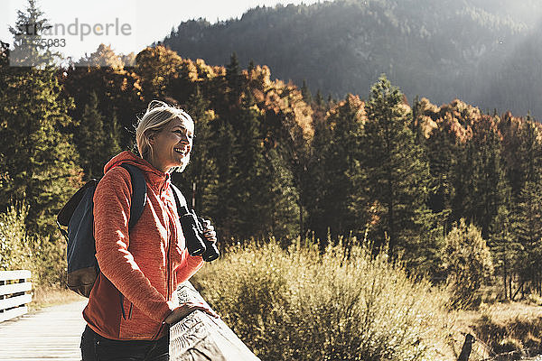 Österreich  Alpen  Frau auf einer Wanderung auf einer Brücke stehend mit Fernglas