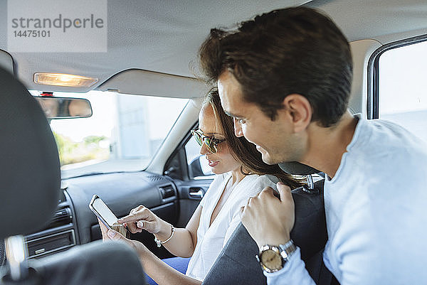 Ehepaar im Auto mit Mann auf dem Rücksitz und Frau mit Handy auf dem Beifahrersitz
