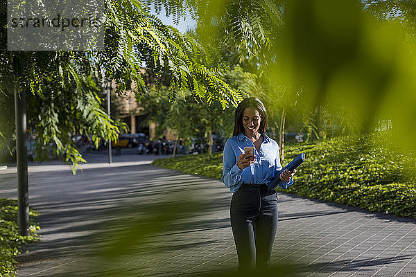 Geschäftsfrau benutzt Smartphone  hält Laptoptasche im Park