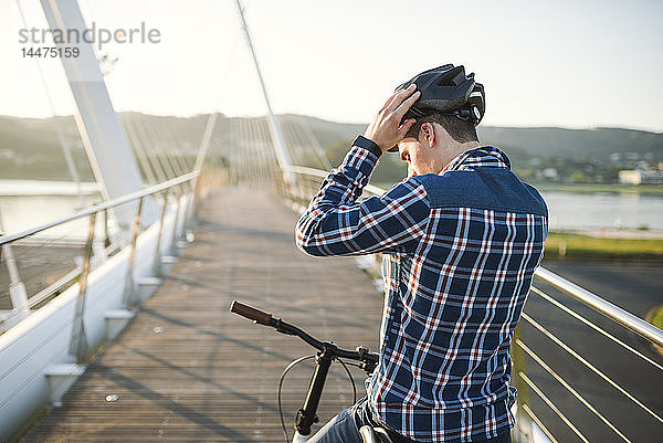 Junger Mann auf Fahrrad  der auf einer Brücke einen Helm aufsetzt