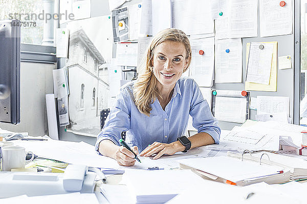 Porträt einer lächelnden Frau  die am Schreibtisch im Büro Papierkram erledigt