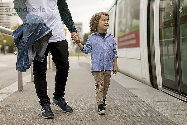 Vater und Sohn gehen Hand in Hand an der Straßenbahnhaltestelle in der Stadt