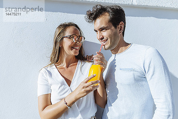 Glückliches Paar  das sich an einem sonnigen Tag einen Orangensaft teilt