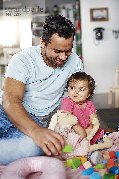 Lächelnder Vater und kleines Mädchen spielen zu Hause mit Bausteinen