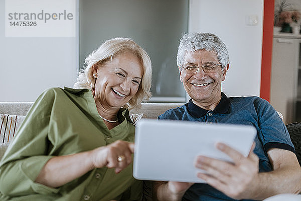 Glückliches älteres Ehepaar sitzt zu Hause auf der Couch und teilt sich ein Tablet