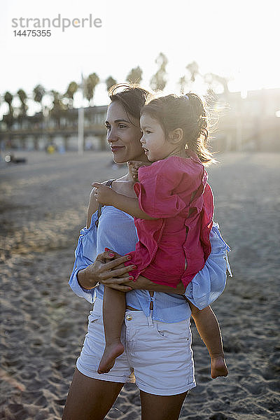Mutter und Tochter stehen bei Sonnenuntergang am Strand