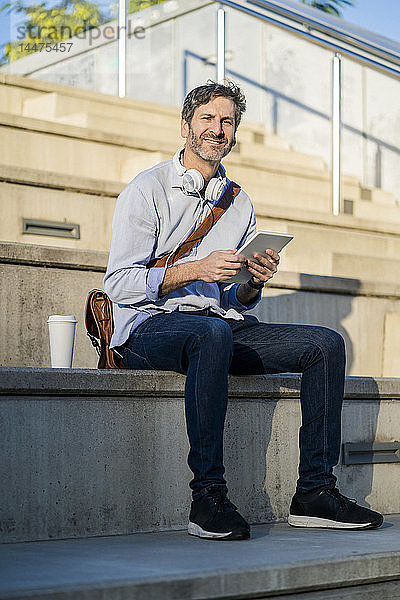 Porträt eines lächelnden  reifen Mannes auf einer Treppe sitzend mit Tablette