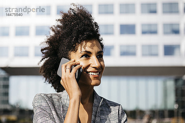 Porträt einer lächelnden Geschäftsfrau am Mobiltelefon vor dem Bürogebäude