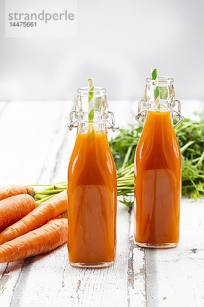 Karotten  Gläser mit Karottensaft und Bügelverschlussflaschen auf Holz