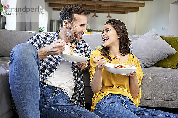 Ehepaar sitzt im Wohnzimmer und isst Spaghetti