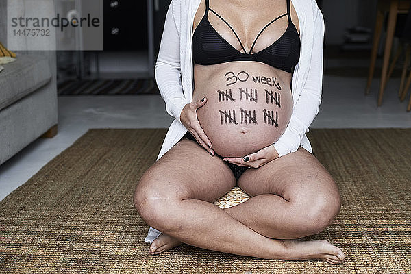 Nahaufnahme einer schwangeren Frau  die zu Hause auf dem Boden sitzt und Striche auf dem Bauch hat