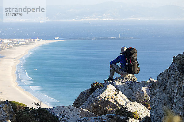Spanien  Andalusien  Tarifa  Mann auf einer Wanderung an der Küste sitzend auf einem Felsen mit Aussicht