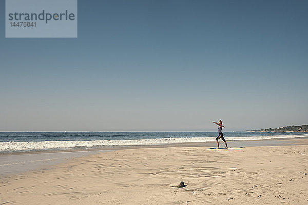 Junge Frau übt Yoga am Strand aus