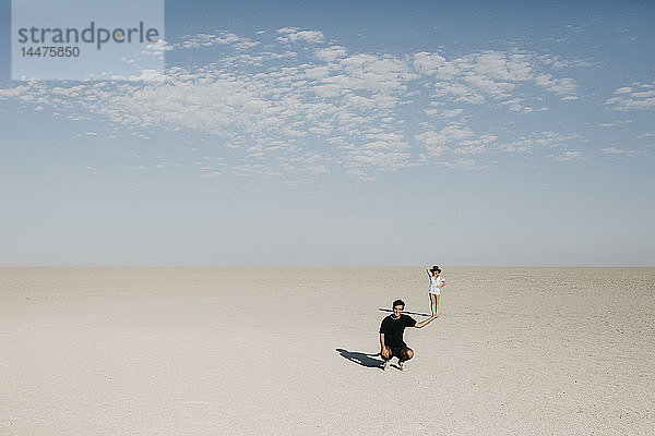 Mann kniet in der Wüste  die Frau scheint auf seiner Hand zu balancieren