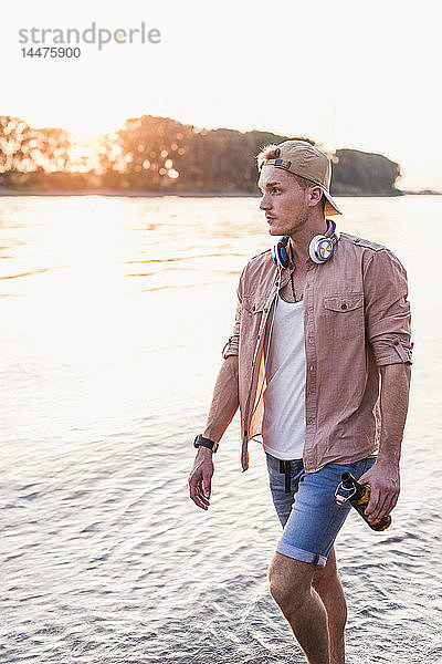 Junger Mann geht bei Sonnenuntergang am Flussufer