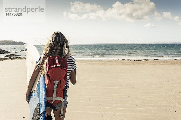 Junge Frau mit Rucksack  Spaziergang am Strand  Surfbrett tragen