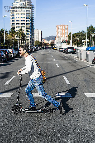 Erwachsener Mann  der mit seinem Kickroller in der Stadt unterwegs ist und eine Straße überquert